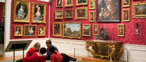 A group of young museum visitors recline in the gallery while discussing the paintings around them.