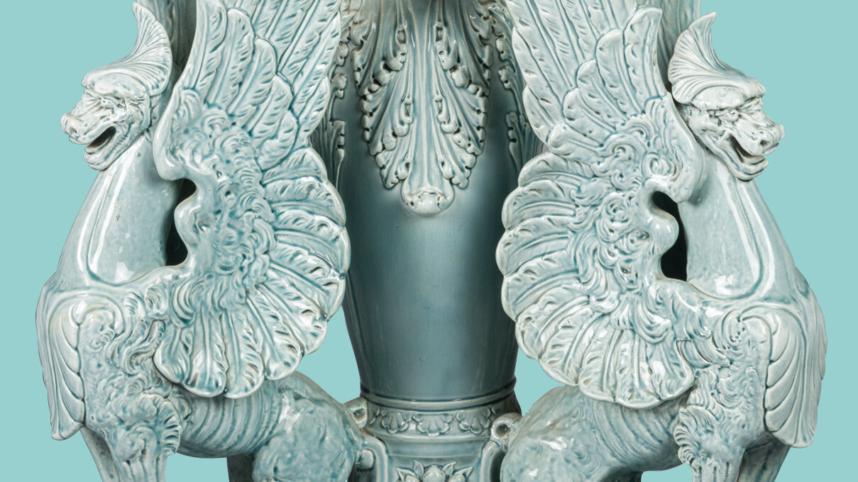 Detail of teal colored cerramic vase flanked by griffins