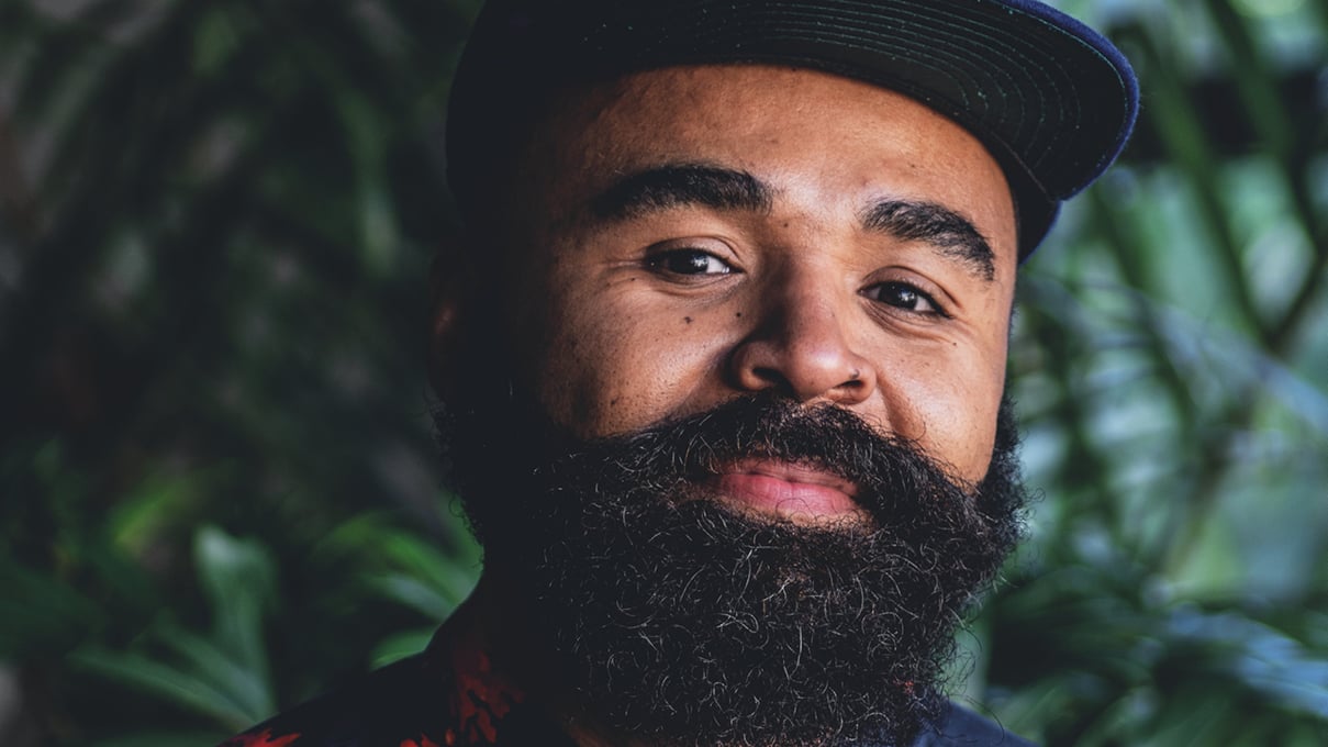 Close-up of Hilton Carter, smiling, wearing a hat, with plants behind him.