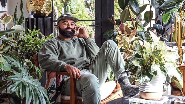 Hilton Carter reclining in a chair surrounded by indoor plants.
