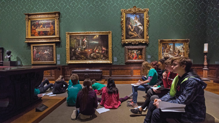 Students sit on the floor and benches of the gallery to study paintings.