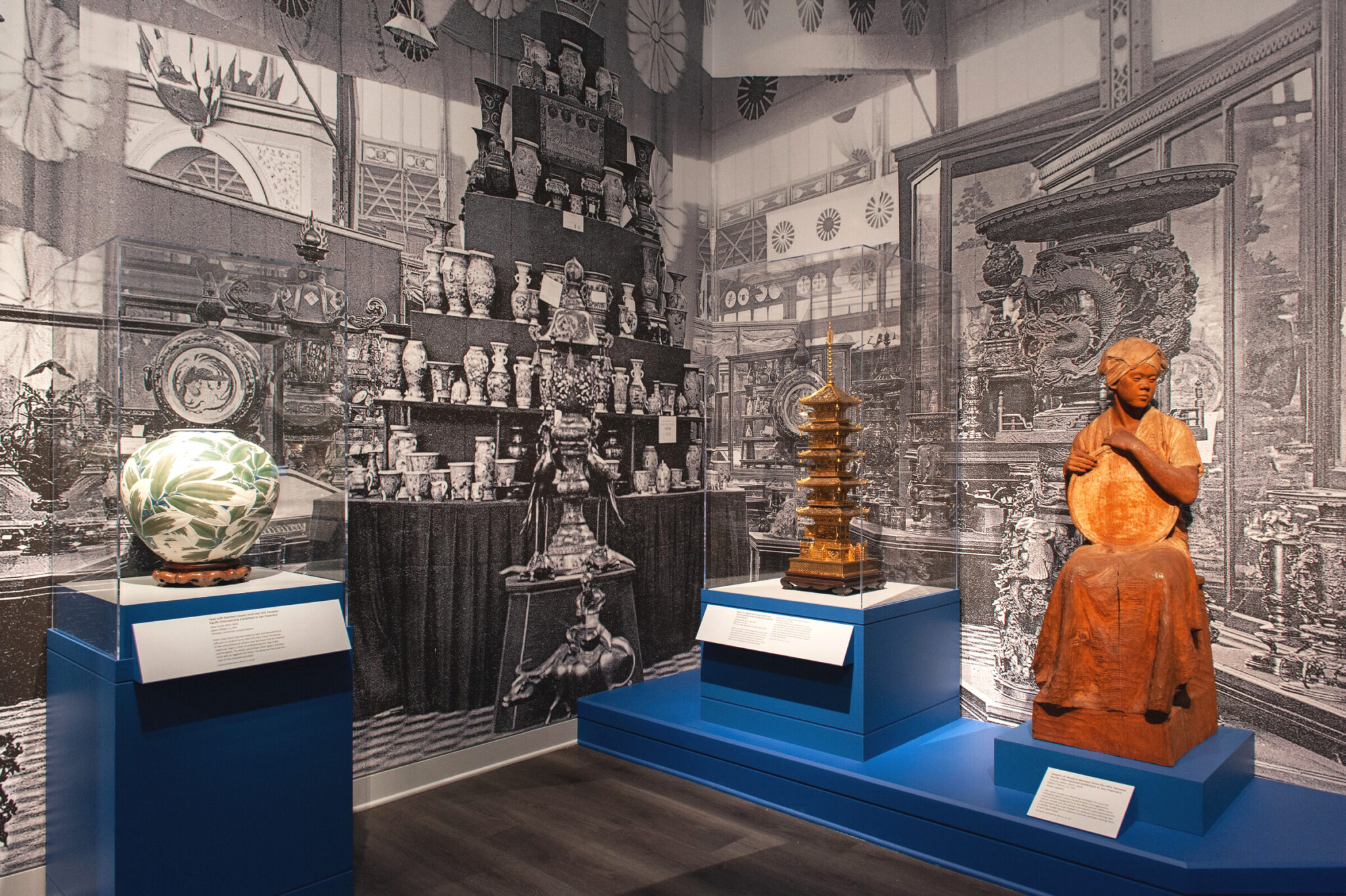 Large wall graphics in the corner of a gallery with several art objects in cases