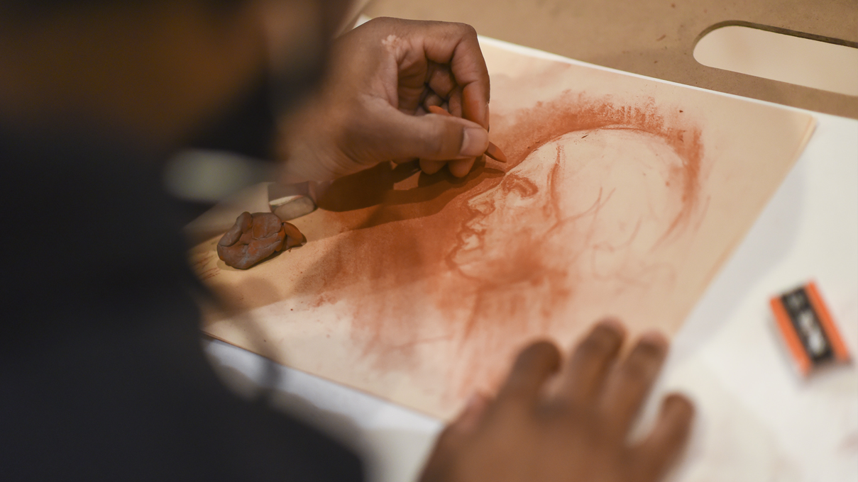 Close-up of a man's hands as he draws a portrait using chalk.