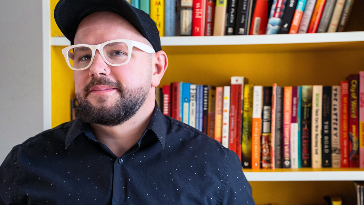 Anthony Moll, wearing white glasses in front of a bookshelf.