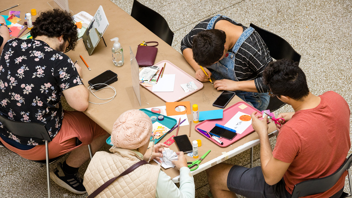 overhead view of several people seated at a table with art supplies, making art together.