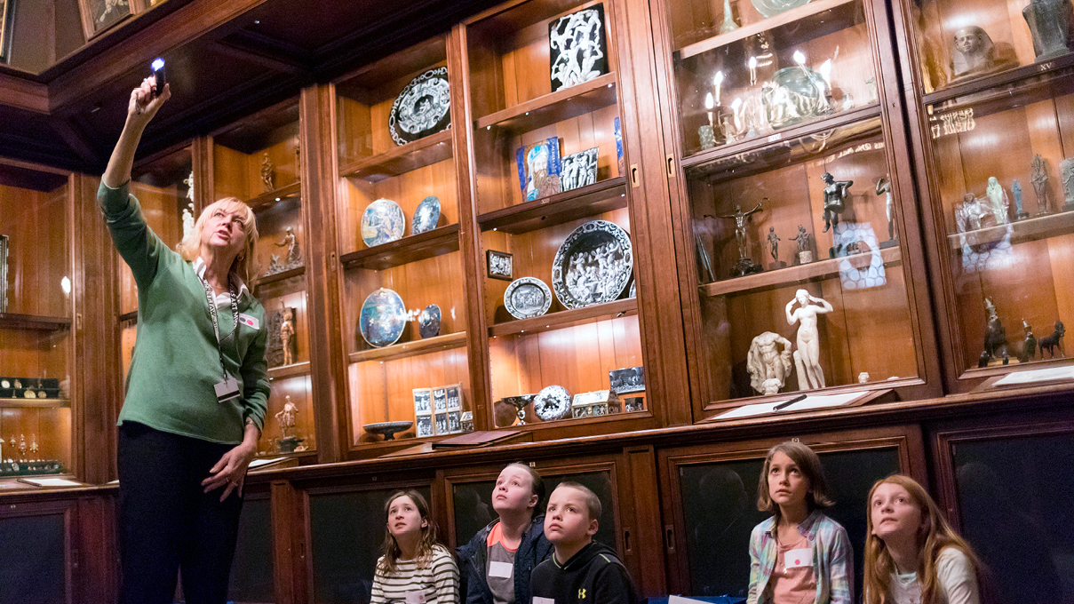 students touring a gallery with wooden shelves of ceramics