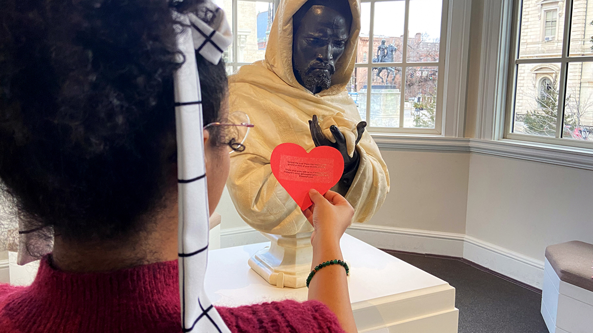 a museum visitor places a red heart-shaped valentine card near a beloved artwork