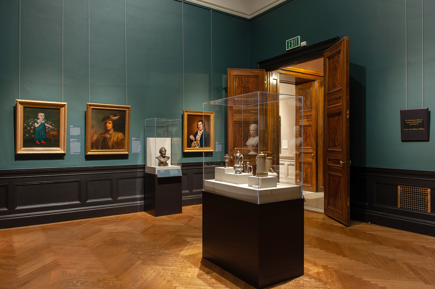 In-gallery view of Selections from the North American Collection: People and Places, which shows art objects in a case, a sculpture, and paintings with a doorway to the side.