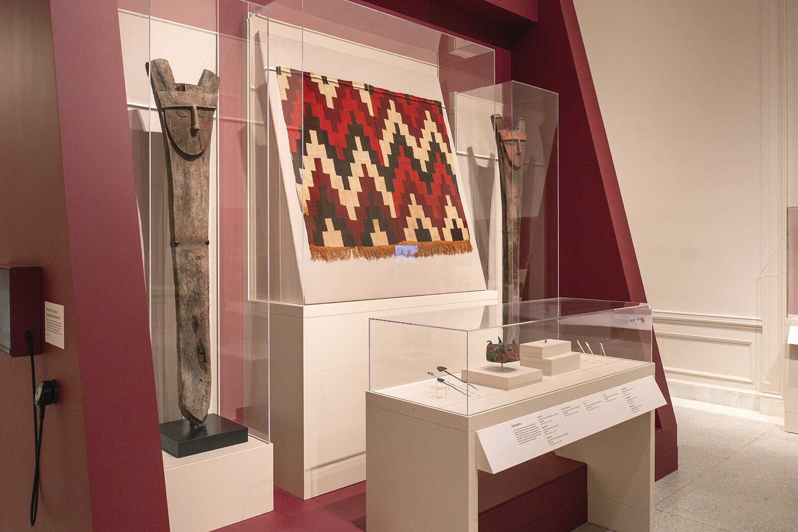 Large wooden carvings stand on either side of a patterned tunic with another smaller display of art objects below