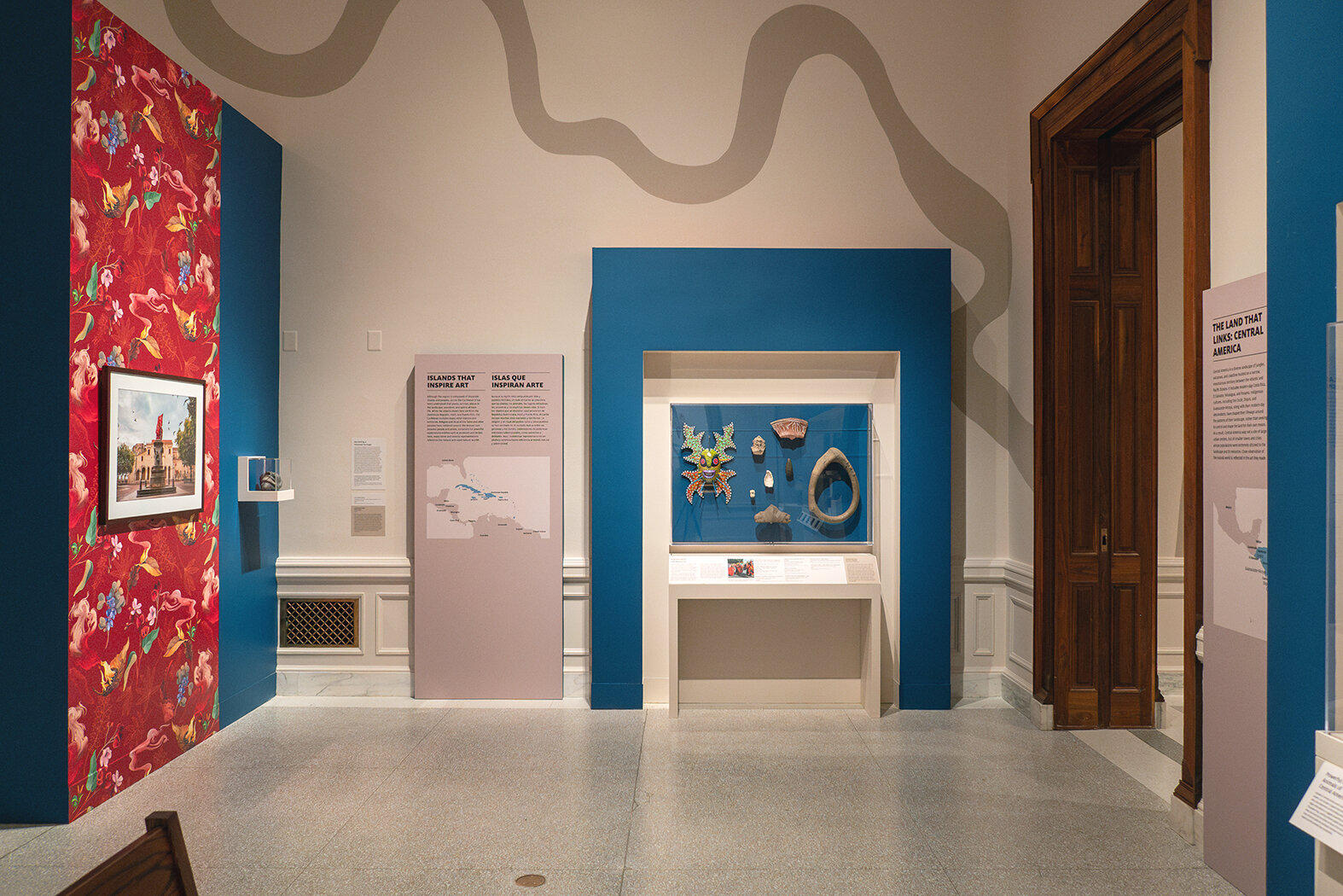 A view of a text panel, case of art objects, and a river pattern on the wall behind