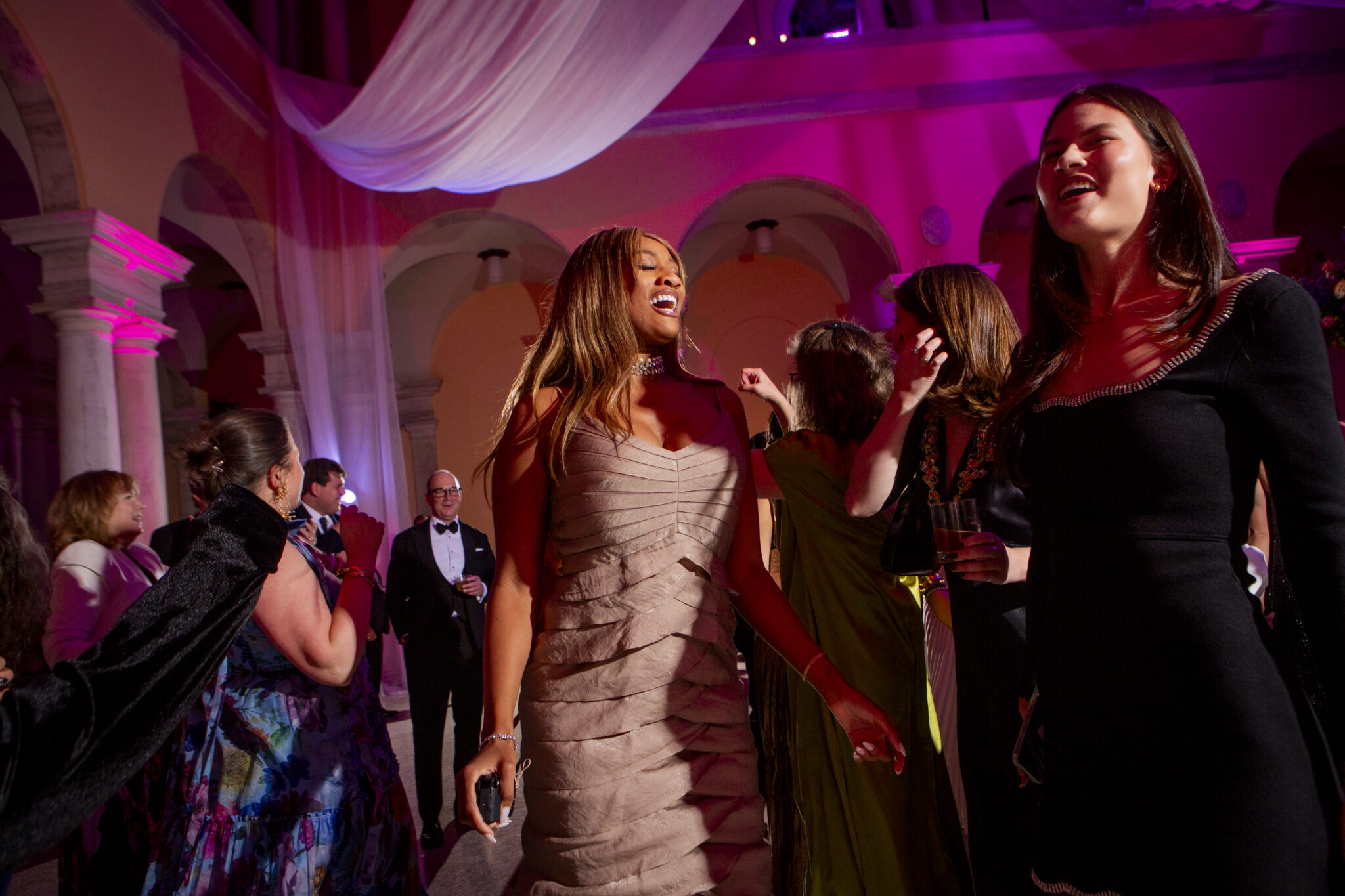 Guests dance and laugh in a pink-lit arcaded court at the 2025 Party.