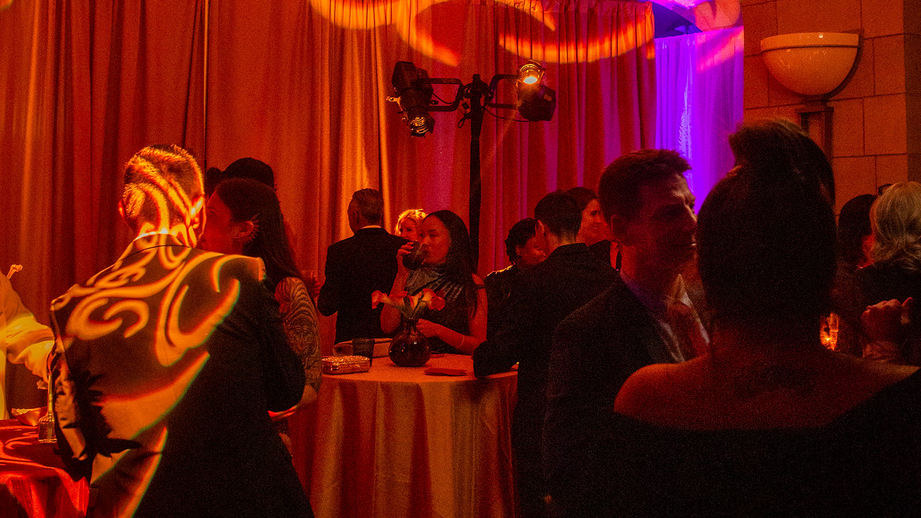 Guests talk around cocktail tables under orange and purple lights at the 2025 VIP Party.