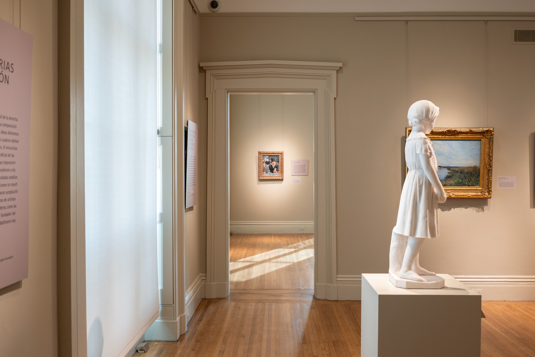 A statue and painting in a gallery in the foreground, with another painting in the room visible in the background