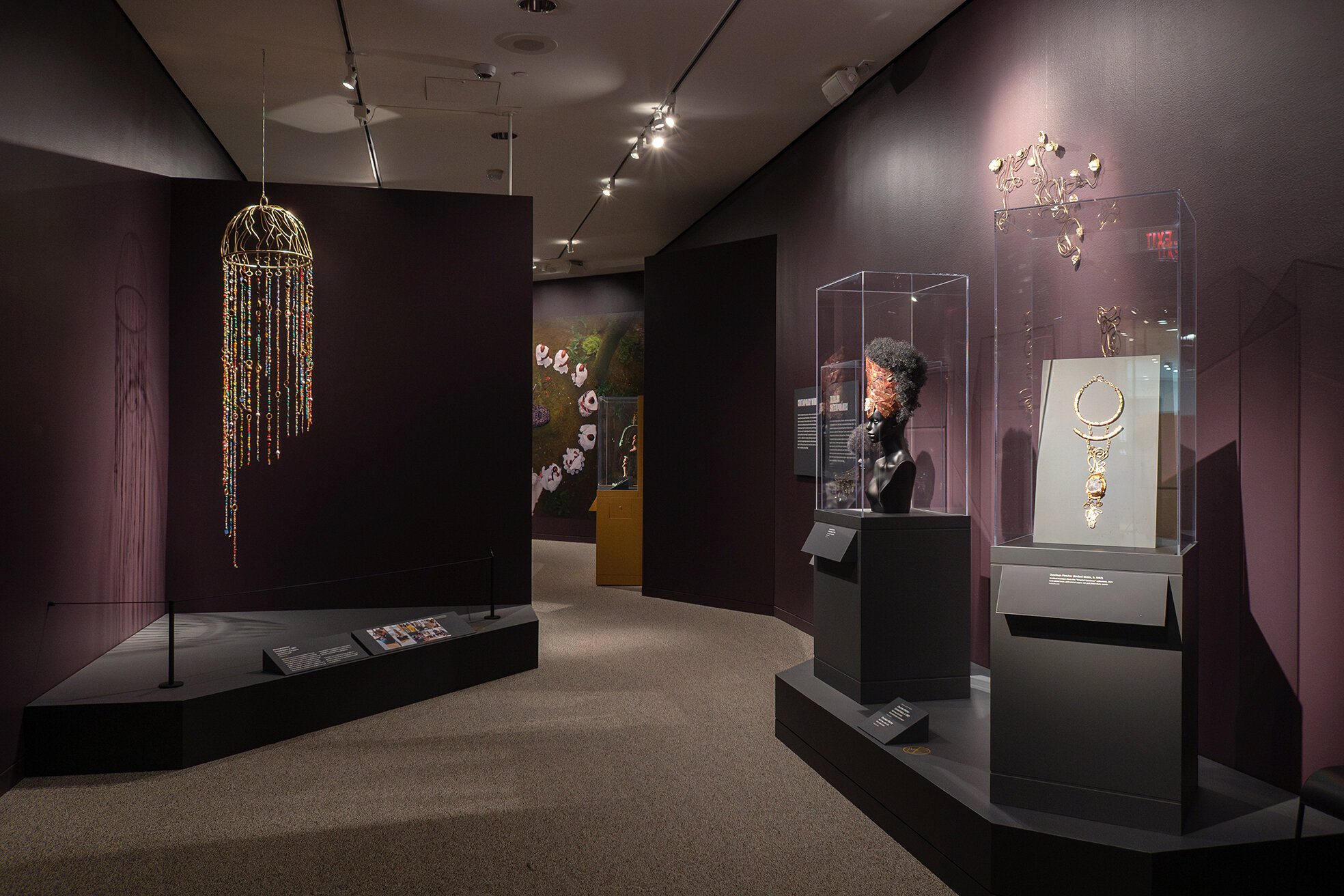 View of gallery with cases and a hanging sculptural artwork in the exhibition Douriean Fletcher: Jewelry of the Afrofuture