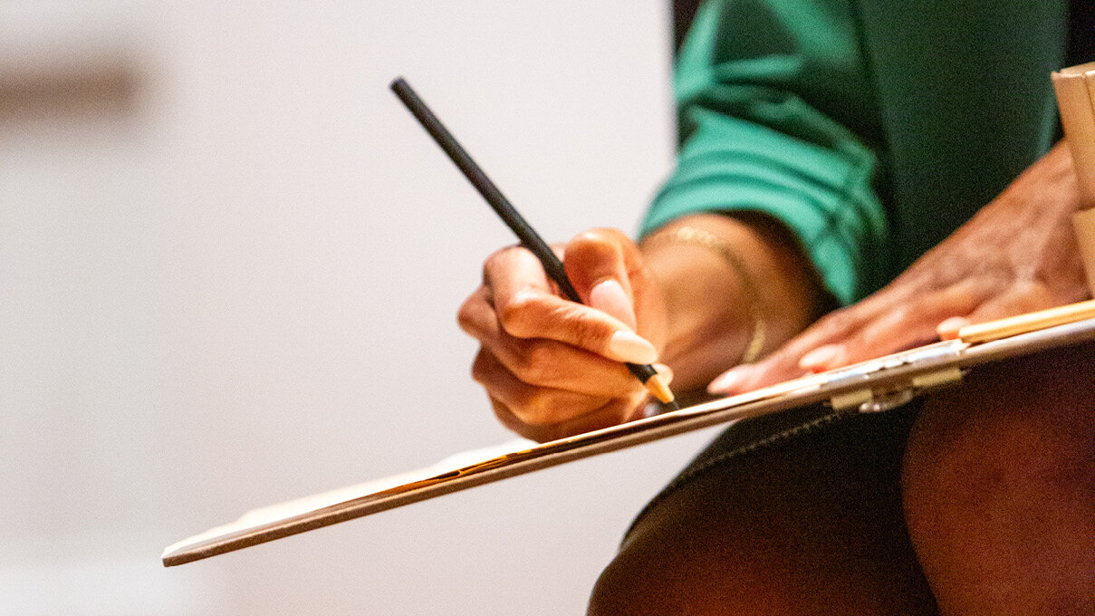 close photo of a hand, pencil, and sketching board, in the gallery