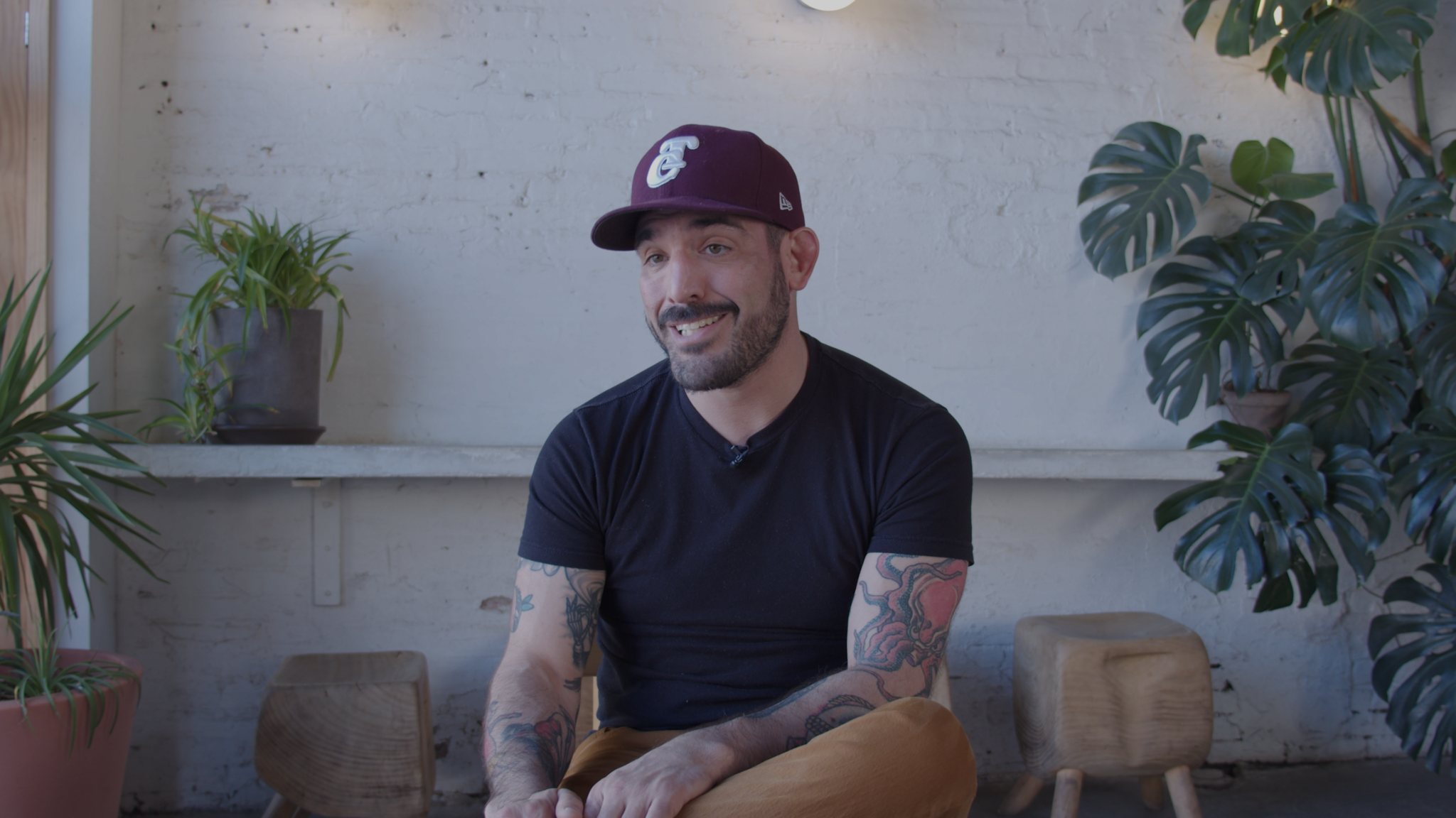 A man in a baseball hat and a black T-shirt smiles at the camera.