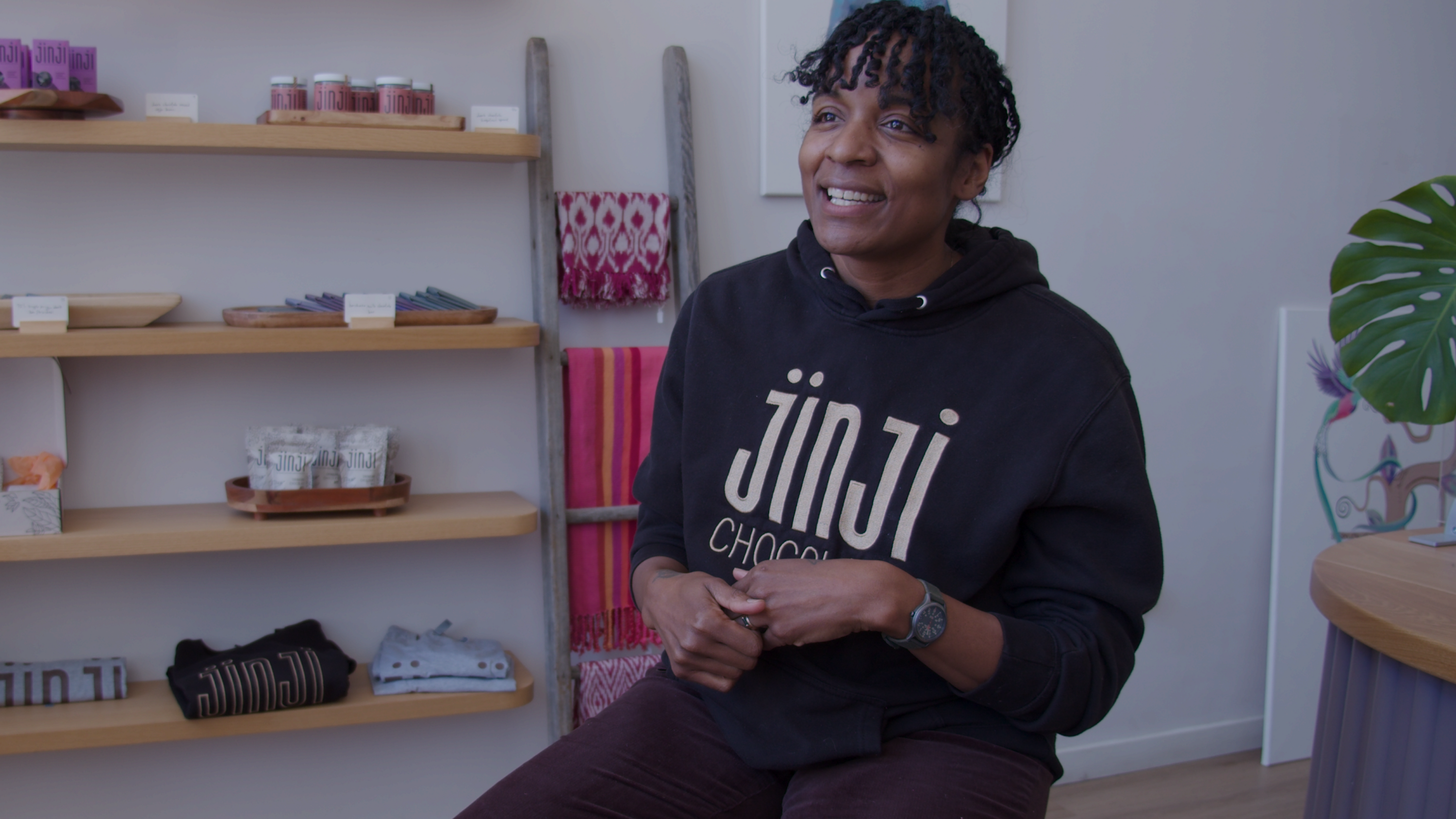 A woman in a black sweatshirt that reads "Jinji Chocolate" smiles at the camera.