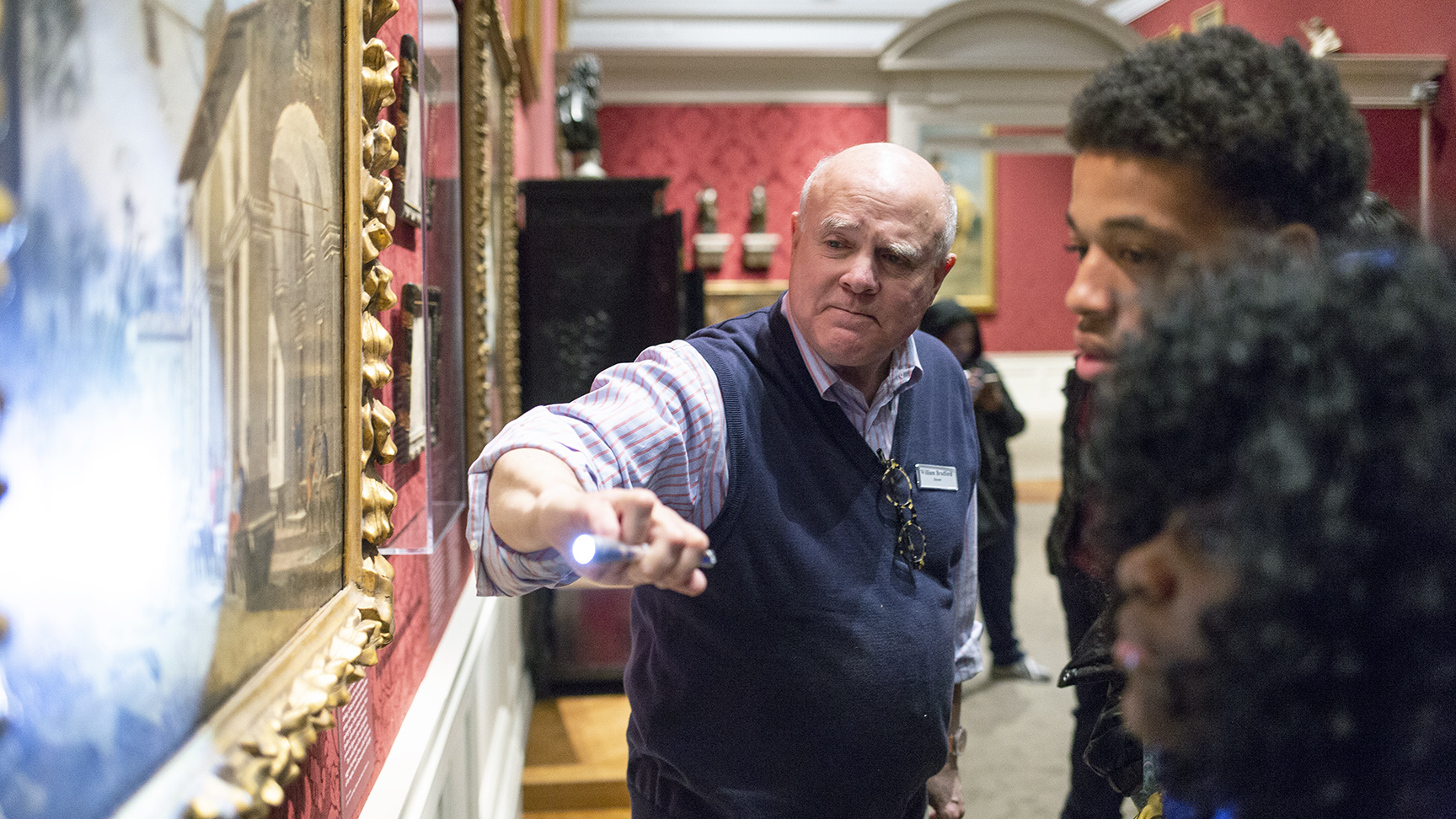 A tour guide points out a detail on a painting using a small flashlight