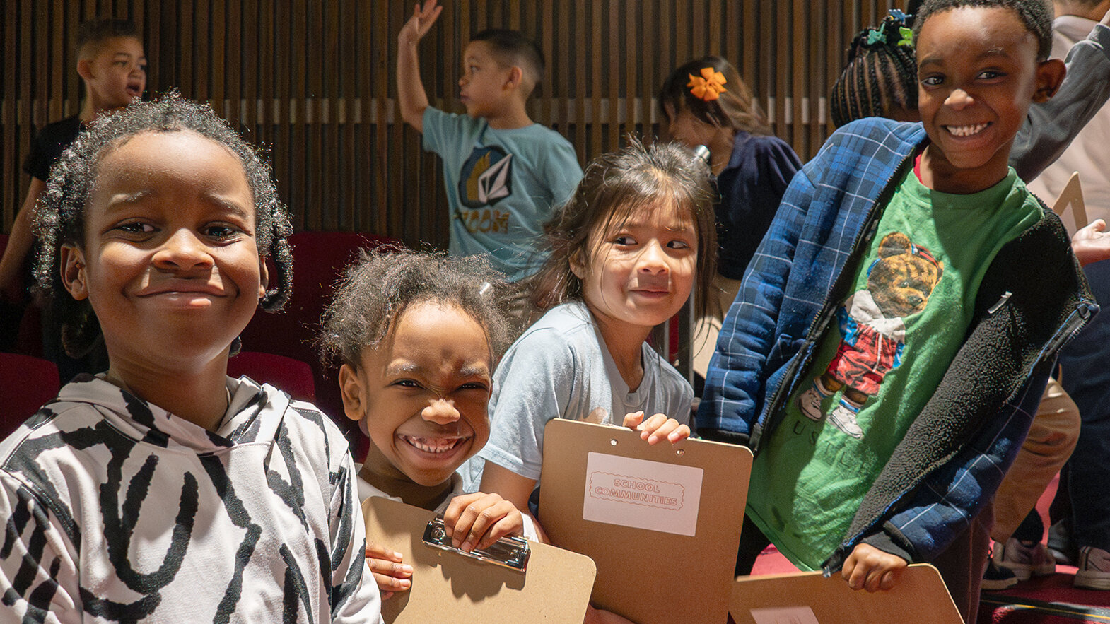 A group of young students on a field trip smile in the auditorium
