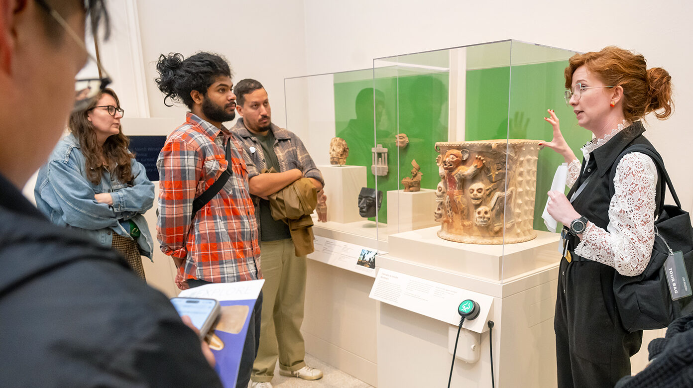 A tour guide leading a large group talks about an art object in a gallery