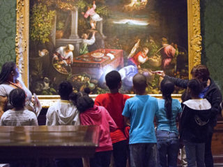 A docent leads a tour for young students, as they discuss a large painting.