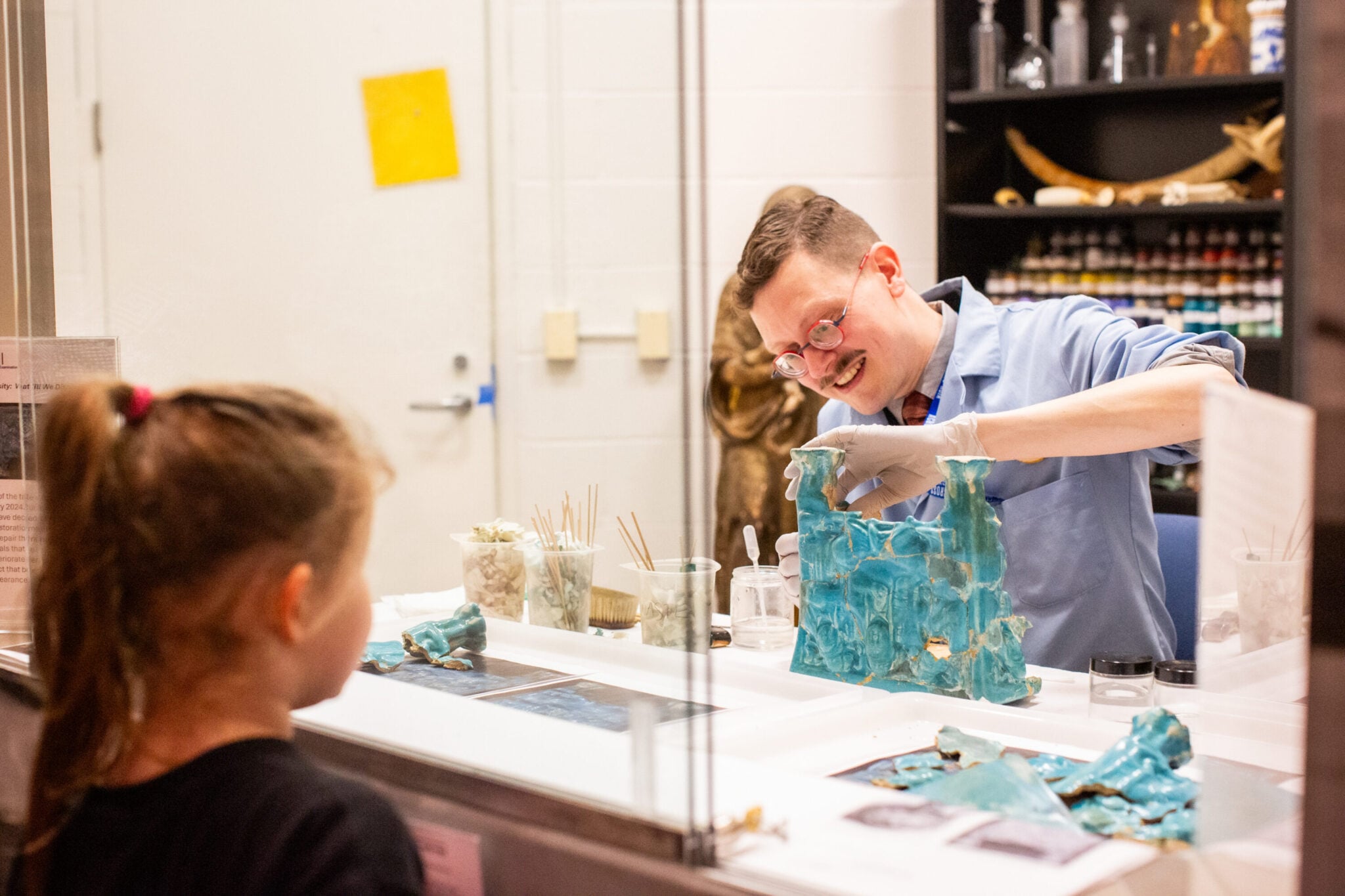 An art conservator works on an object while a visitor observes